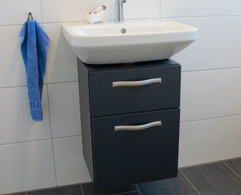 Waschbecken-Unterschrank in eleganter anthrazitfarbener Matt-Optik mit Edelstahl-Griffleisten.