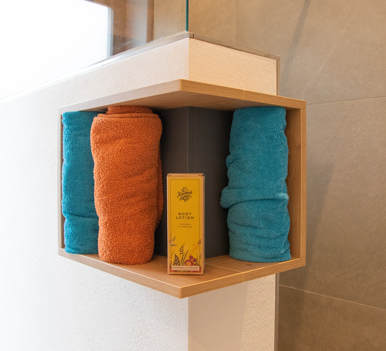 Durch das Eckregal an der Duschmauer sind Nachfüllflaschen und Handtücher stets griffbereit.