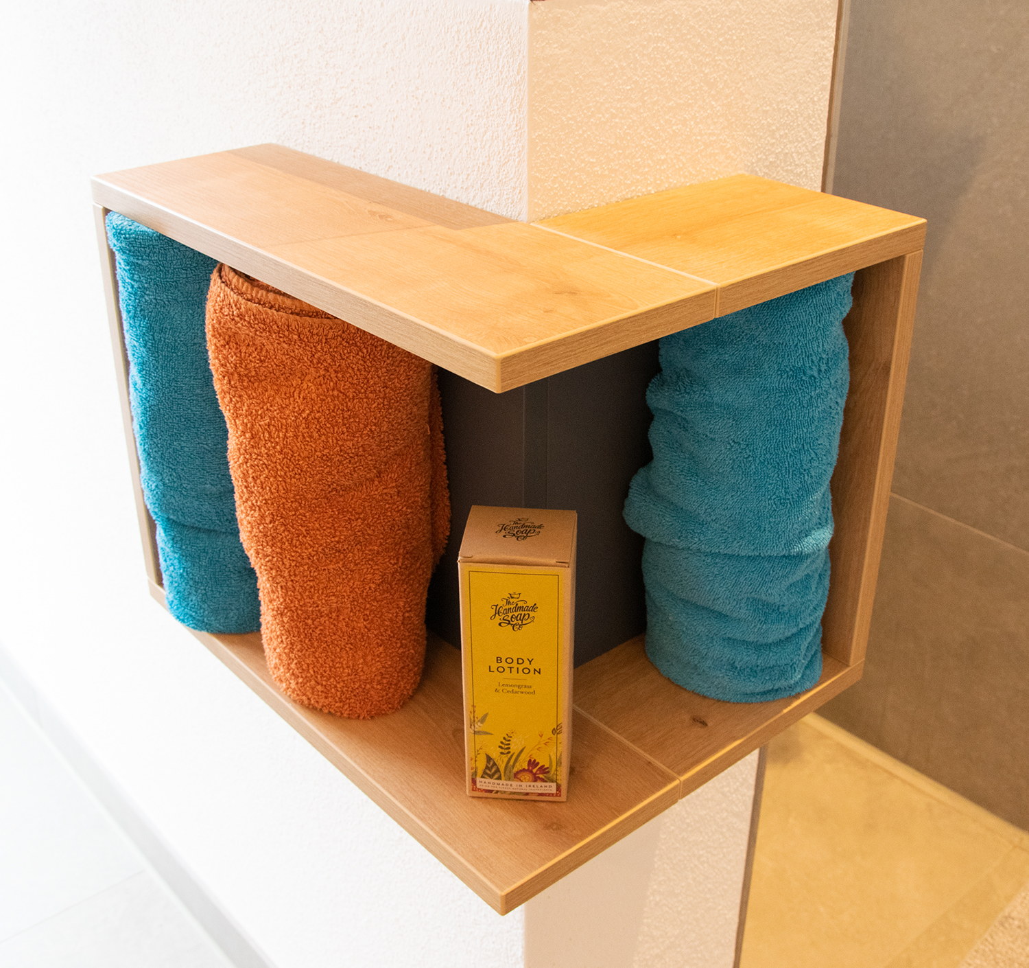 Durch das Eckregal an der Duschmauer sind Nachfüllflaschen und Handtücher stets griffbereit.
